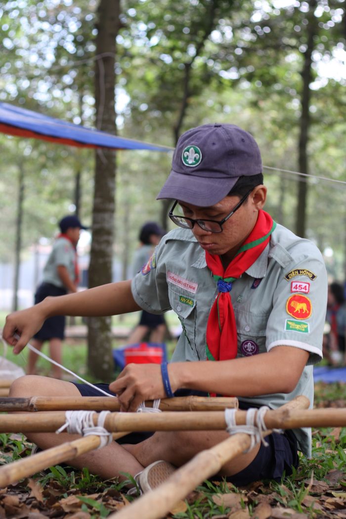 Scout in uniform practicing knot tying during outdoor camping activities.