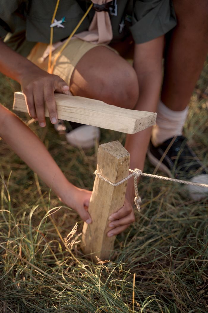 Children working together to hammer a wooden stake during a summer camp activity.